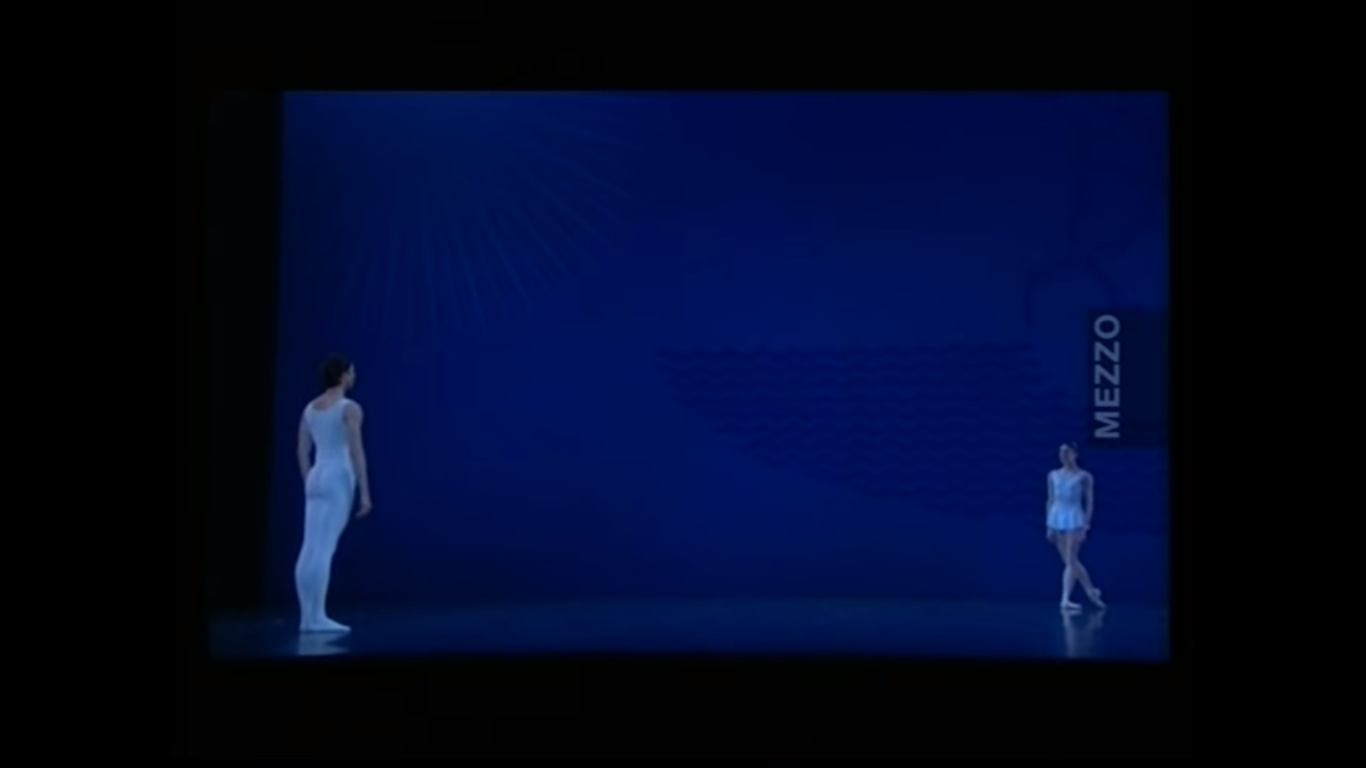 Um palco vazio com fundo azul. Um homem e uma mulher, vestidos de branco, acabaram de se defrontar